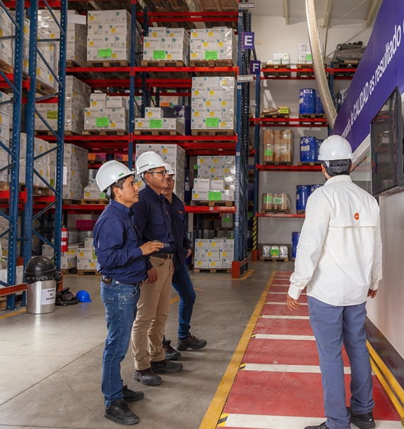 Equipo de Agrow con cascos de seguridad recorriendo el almacén de productos agrícolas entre estanterías